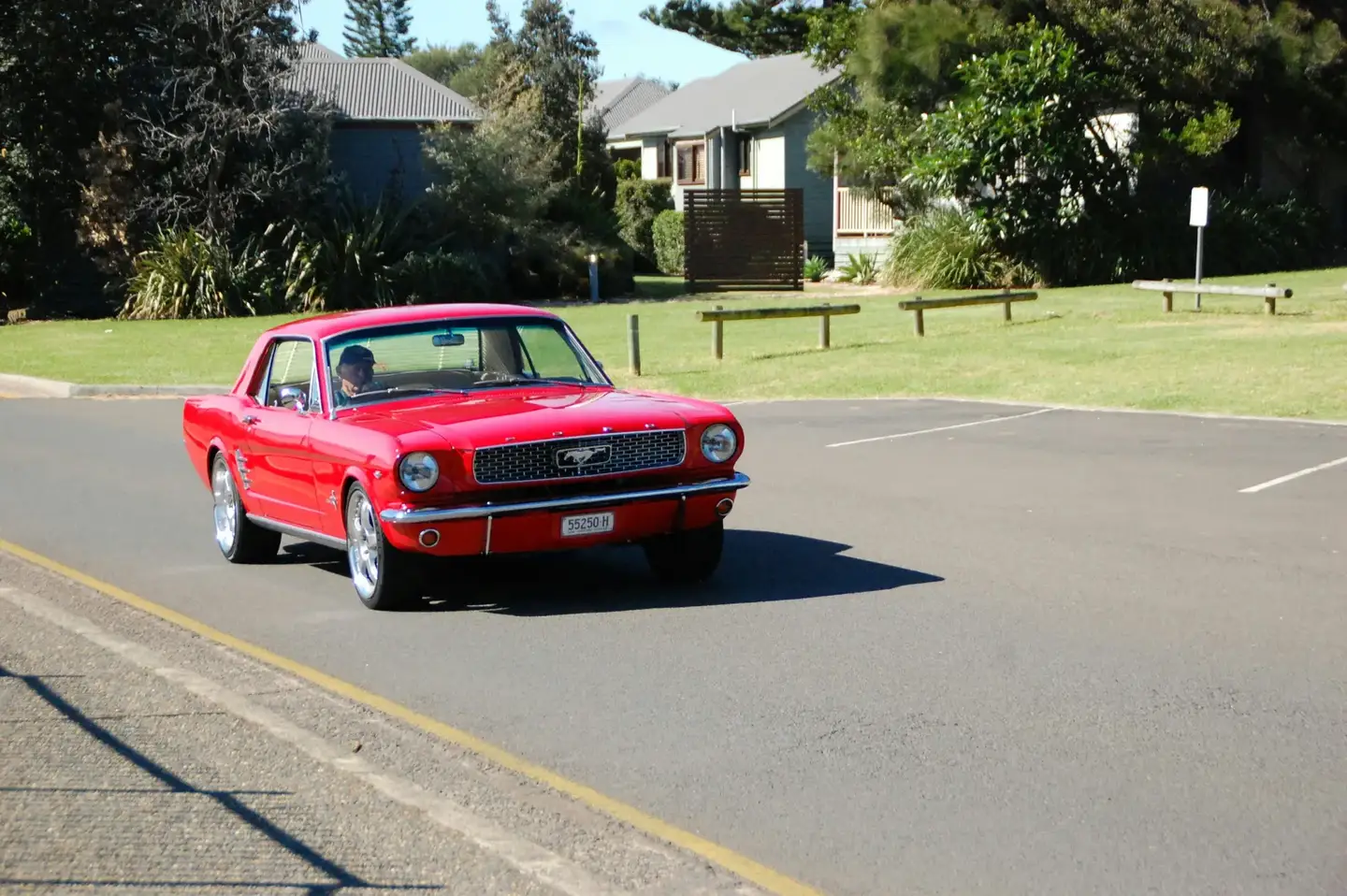A red 1960s Mustang on club plates driving through a Victorian suburb